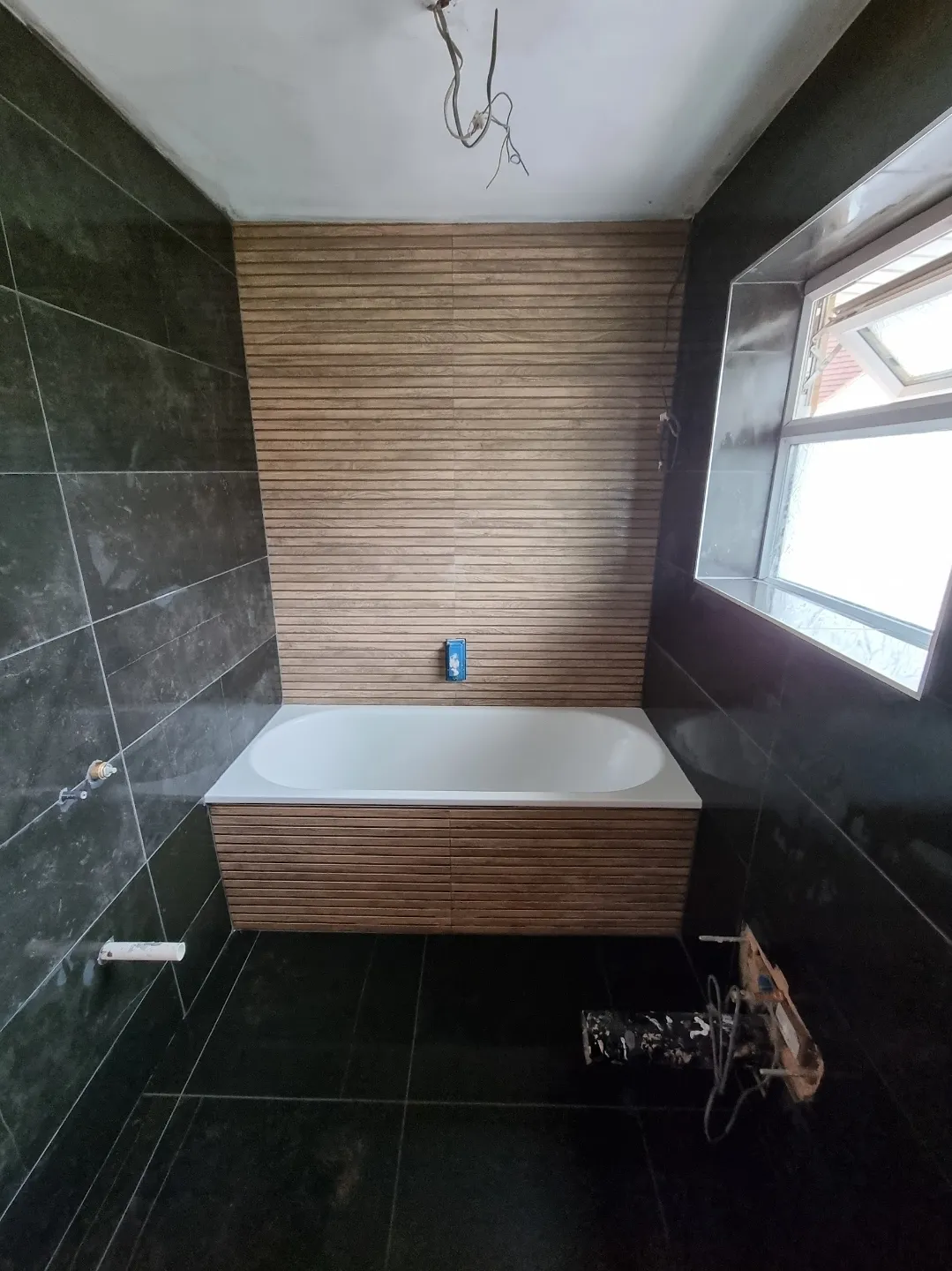 Bathroom black marble tiles with bath and timber slat panel in progress — bathroom fitters Surrey