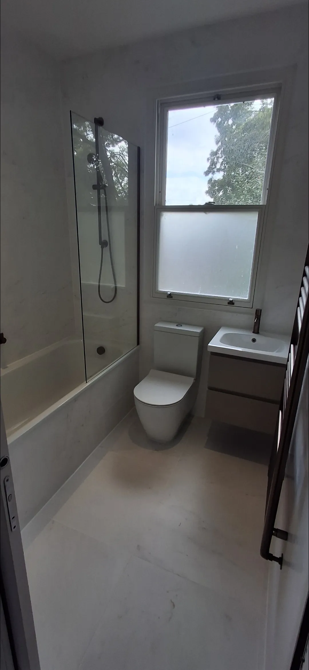 Bathroom with white marble effect tiles completed — bath, toilet and vanity — bathroom fitters Surrey