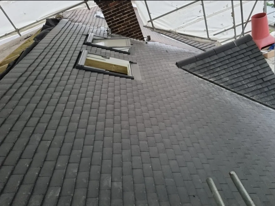 Dark slate effect tile roof with Velux under scaffold tent — roofers Surrey